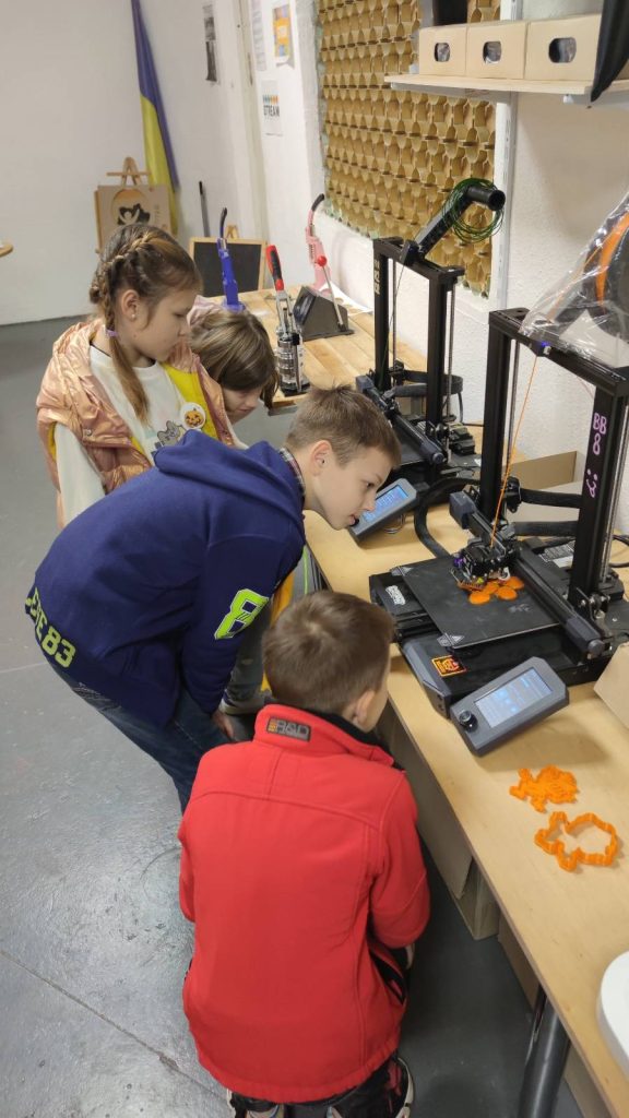 На фото діти спостерігають за роботою 3d принтера
